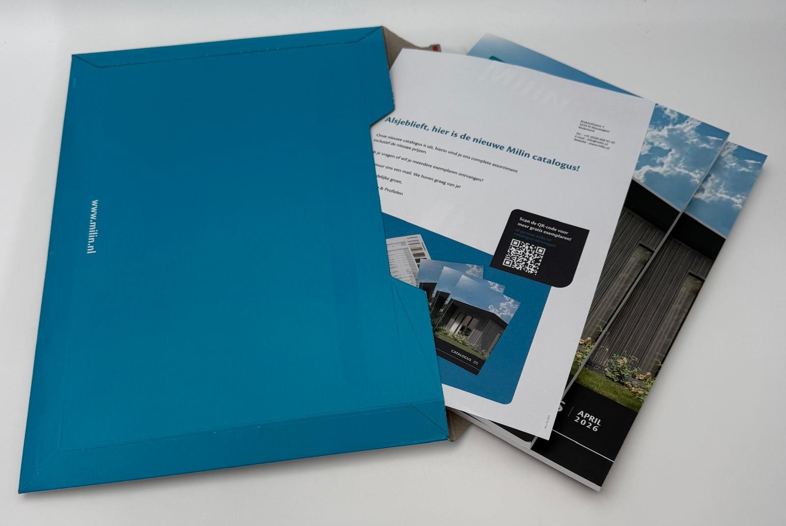 Een blauwe envelop waaruit brochures en papieren gedeeltelijk naar buiten steken, waaronder een catalogus met afbeeldingen van moderne gebouwen en een QR-code die op een van de pagina’s te zien is.